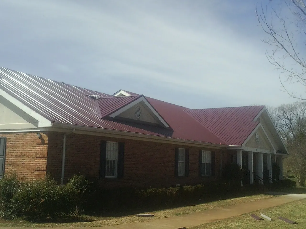 Red metal roof with gabled entries on a long brick building, from a Hail Damage Roof Repair job in Lake Ariel