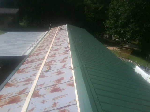 Old rusted panels beside newly installed green metal roofing — Wind Damage Roof Repair by Roofing Brothers in Lake Ariel