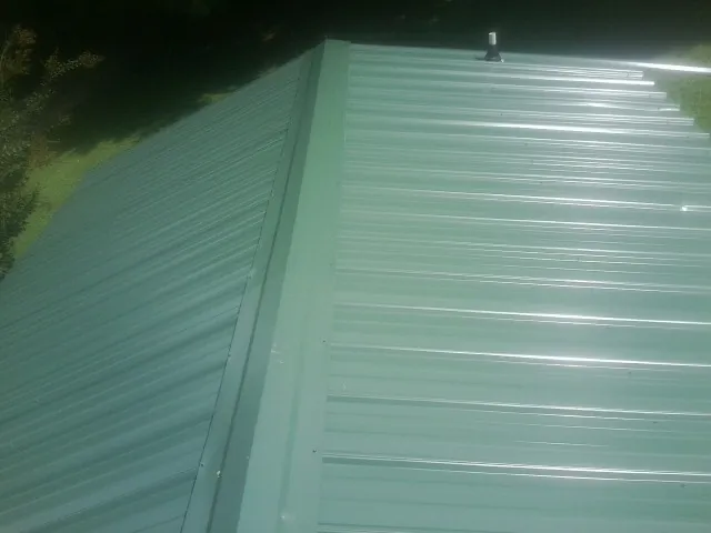 New green metal panels meeting at the ridge of a roof — Flat Roof Repair work by our crew in Lake Ariel