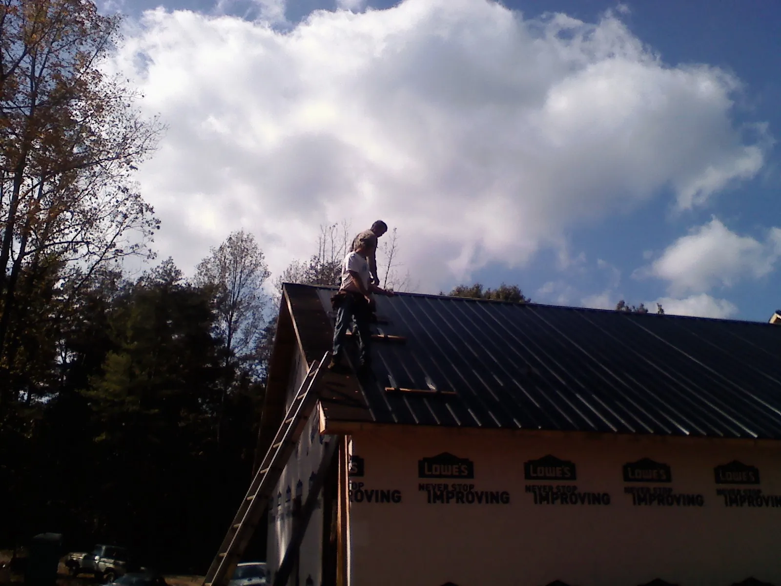 Roofer fastening dark metal panels high against a cloudy sky, from a Roof Inspection job in Lake Ariel
