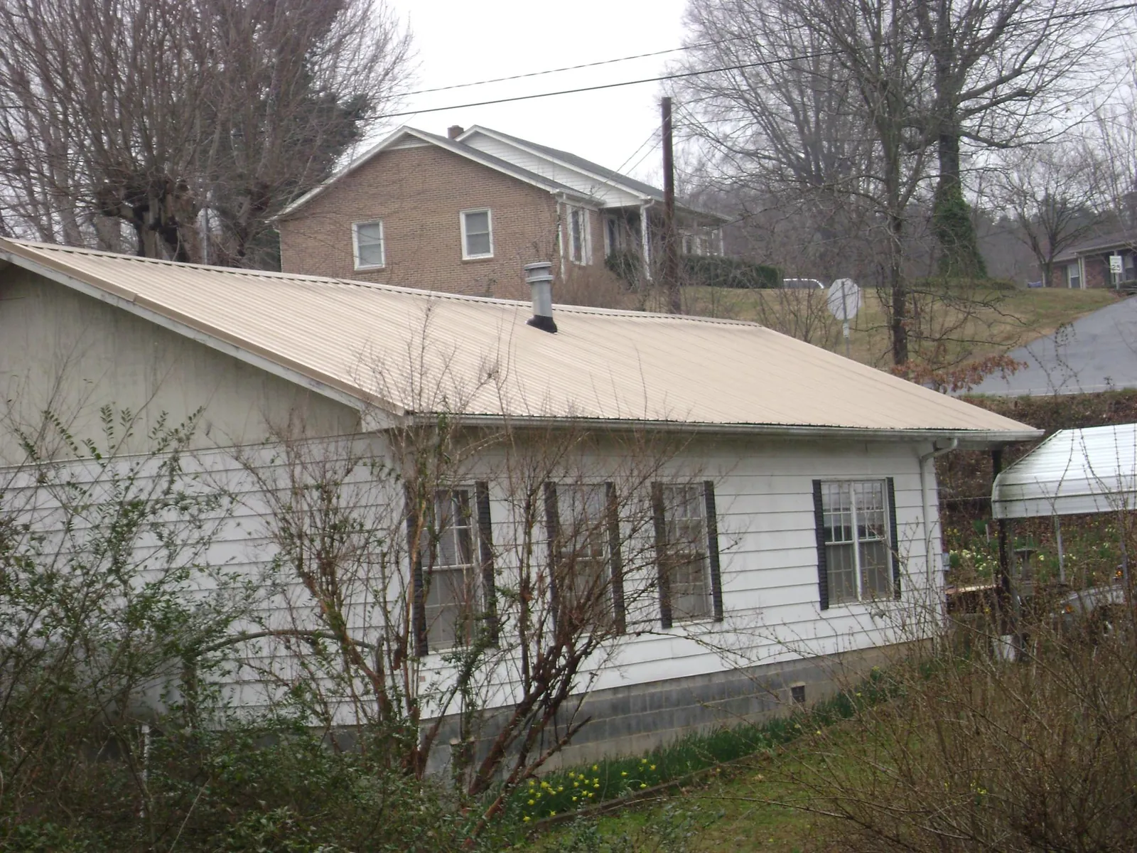 Tan metal roof on a white sided house set into a hillside — Commercial Roofing by Roofing Brothers in Lake Ariel