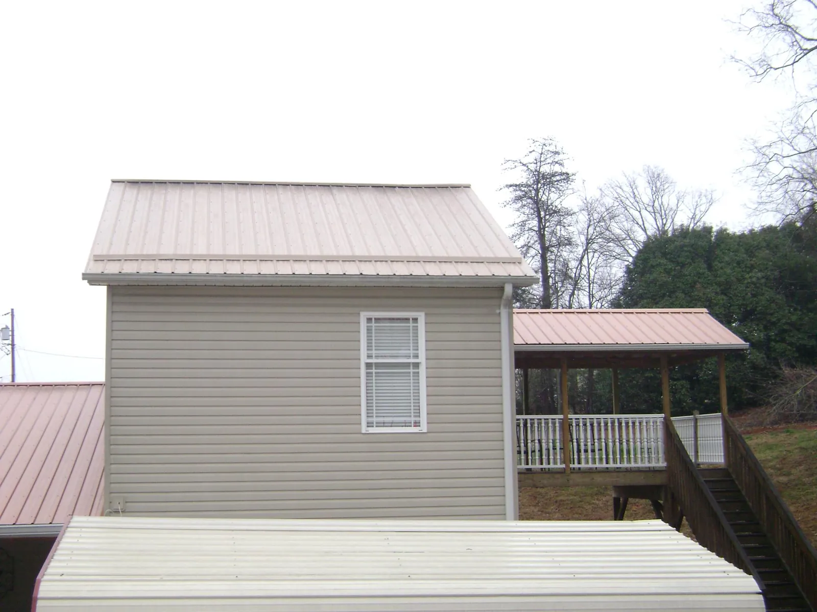 Tan metal roofs on a two story addition and attached porch, from a Roof Replacement job in Lake Ariel